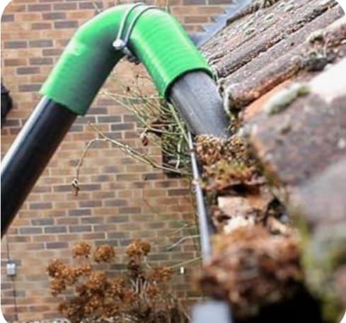A gutter vacuum hose lifting moss and debris out of a blocked gutter
