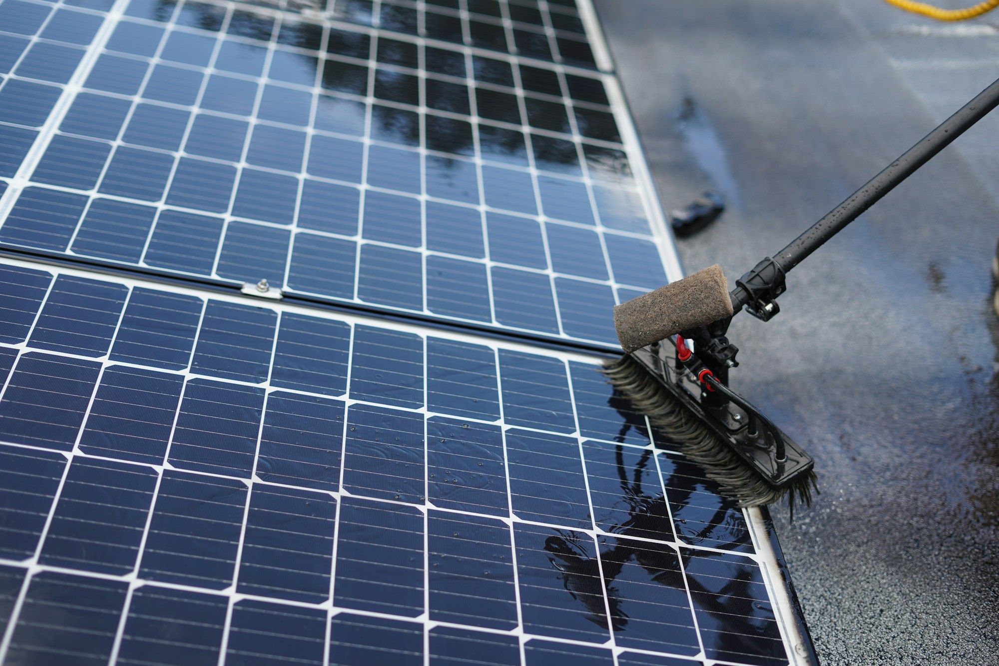 Rooftop solar panels being washed with a soft brush on a long water-fed pole